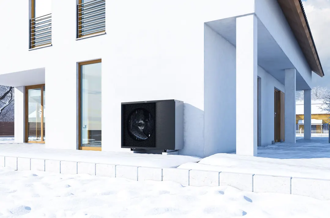 Schwarze Luft-Wasser-Wärmepumpe an der Hauswand eines Neubaus im Winter